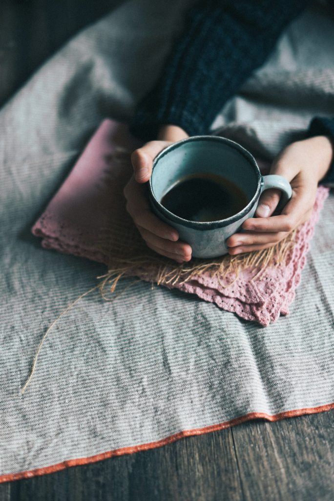 Hands holding a green mug on a soft blanket