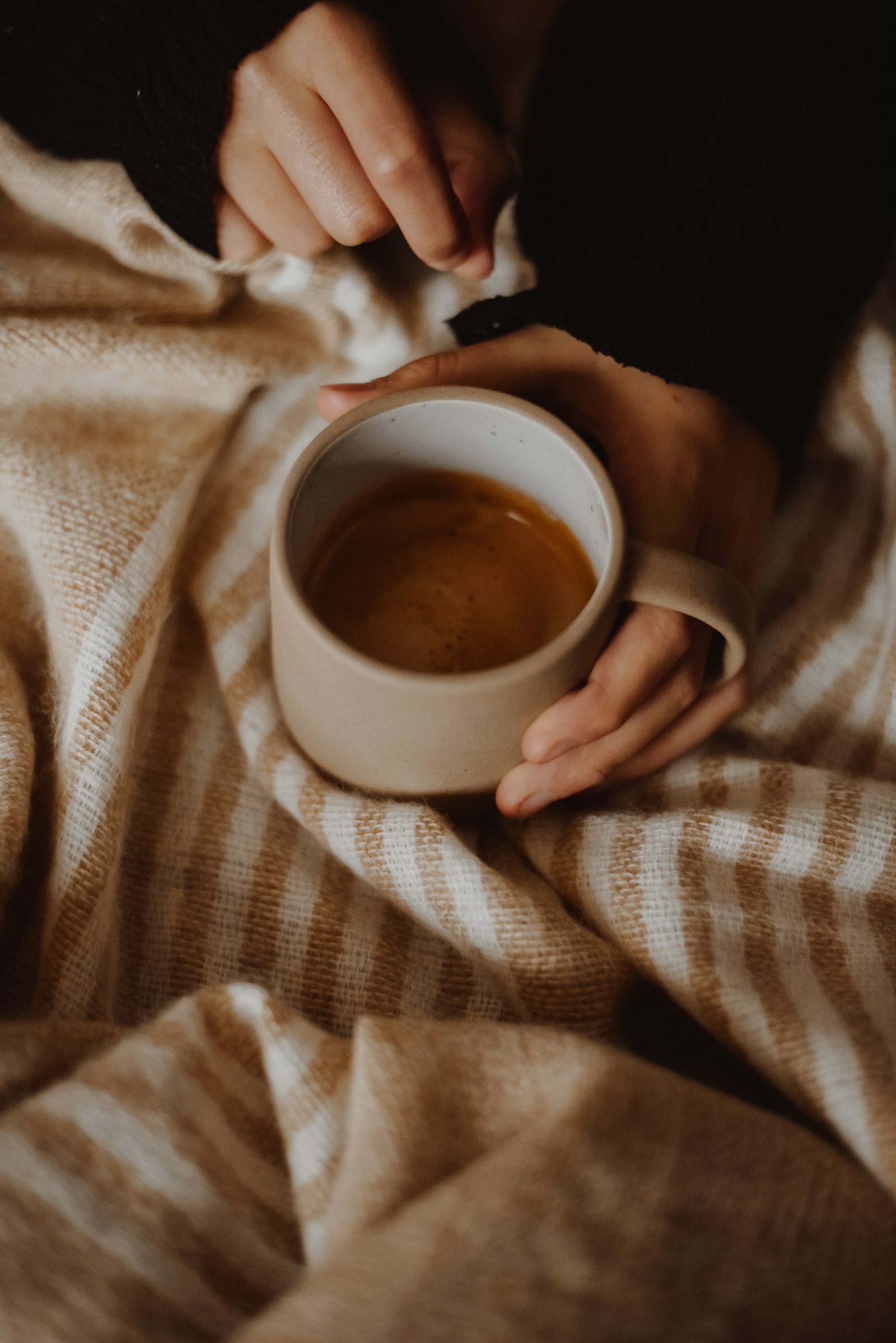 Hands holding a warm mug wrapped in a knit sweater