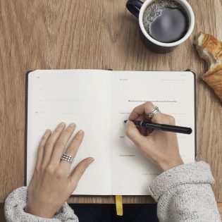 Hands writing in a journal beside a cup of coffee